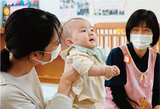 赤ちゃんを抱っこする母親と保育士の画像