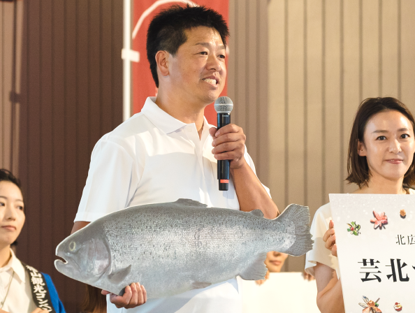 魚のパネルを持ち、マイクを持って演説をする男性の写真