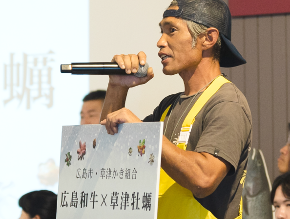 マイクとパネルを持ち、演説をするキャップを着用した男性の写真