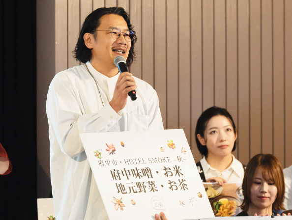 マイクとパネルを持ち、演説をするメガネをかけた男性の写真