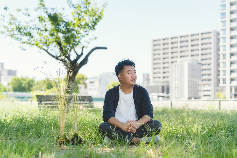 川辺の芝生の上に座り横向きに微笑む男性