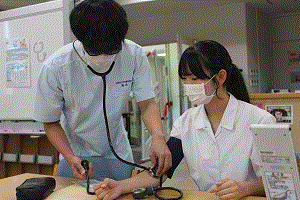 看護学生が高校生に血圧測定をしている。