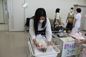 高校生がベビー人形を恐る恐る抱っこしようとしている。