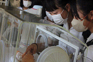 高校生がベビー人形にそっと触れている